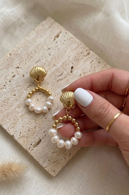 Gold and pearl earrings held by a hand on a textured surface
