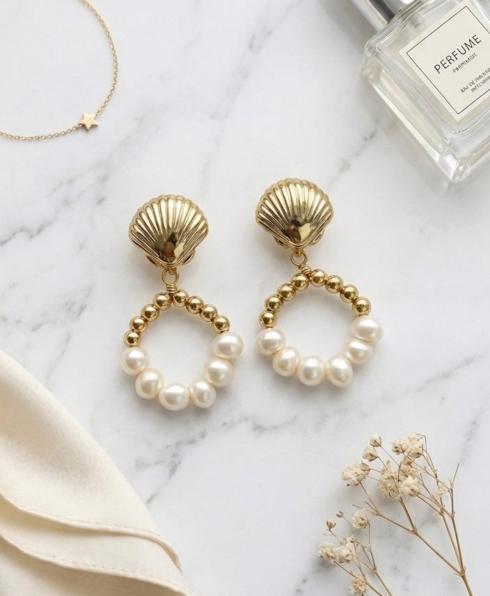 Gold earrings with pearls on a marble surface with a perfume bottle and fabric.