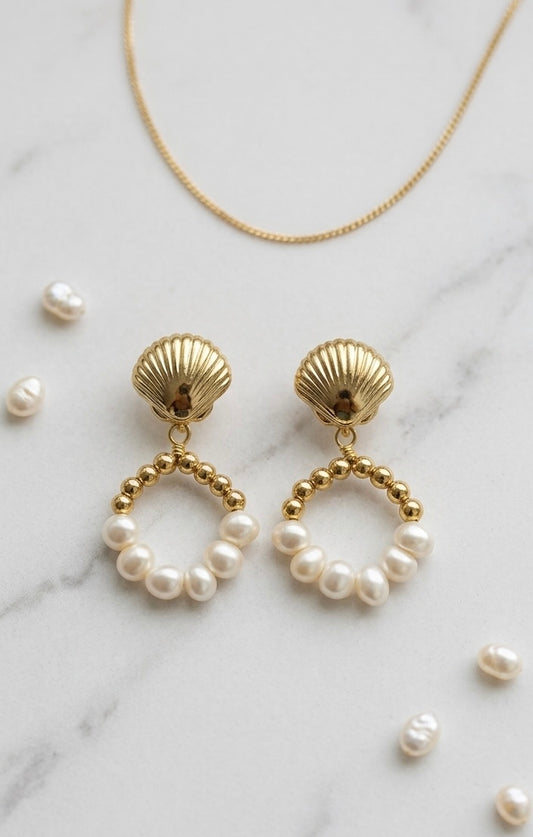 Gold shell earrings with pearl beads on a marble surface