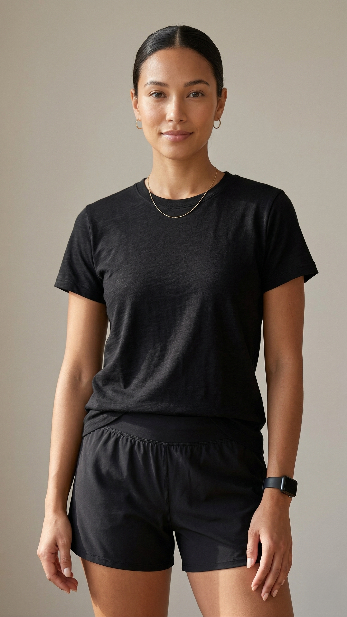 Woman wearing a black t-shirt and black shorts against a neutral background