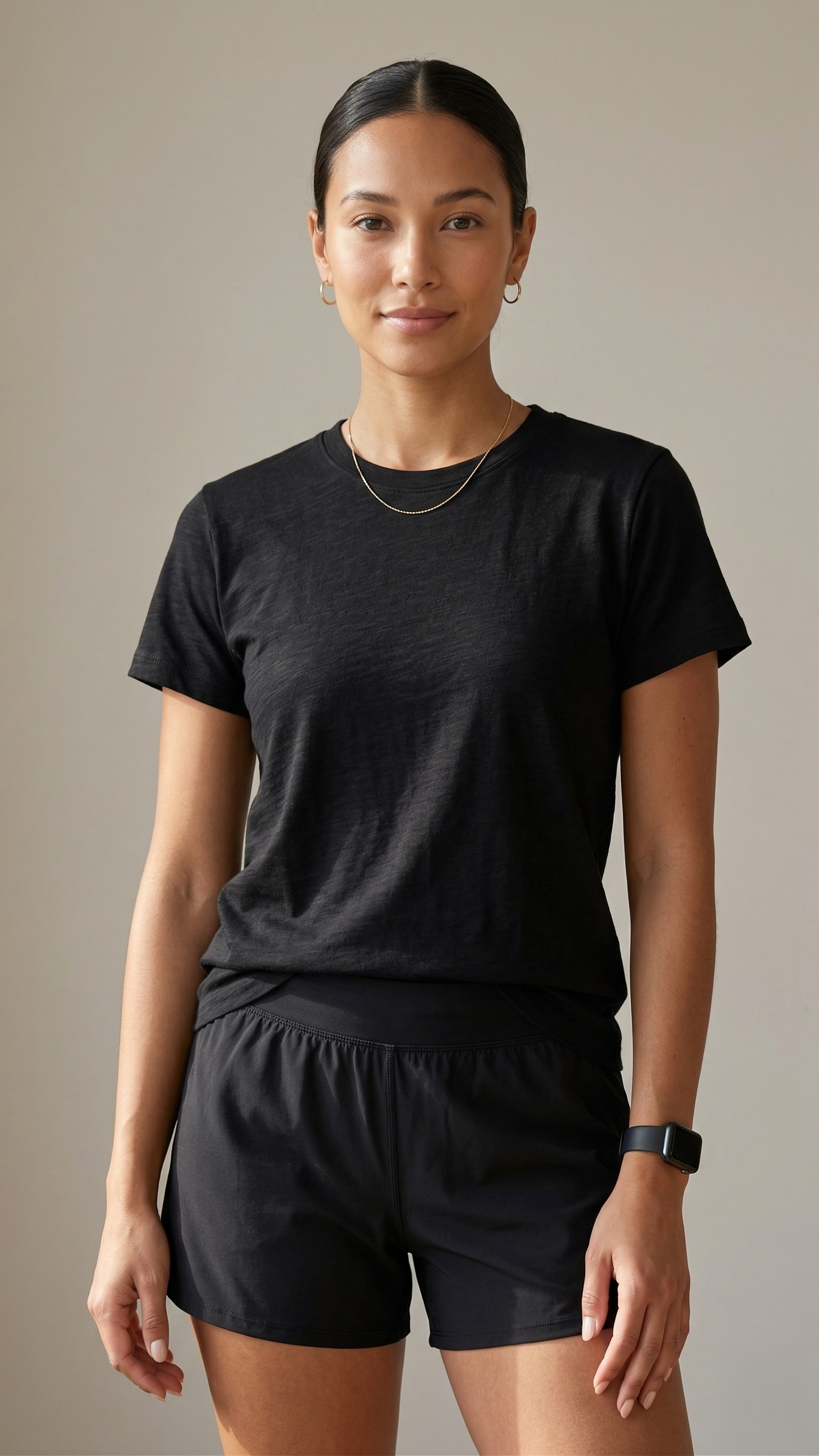 Woman wearing a black t-shirt and black shorts against a neutral background